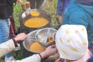 Kinder und eine Frau passieren Kürbissuppe mit der Flotten Lotte am Lagerfeuer