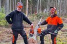 2 junge Männer in Motorsägenschutzkleidung halten eine Motorsäge