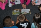 Kinder liegen mit Lehrerin um ein Bilderbuch, es wird vorgelesen